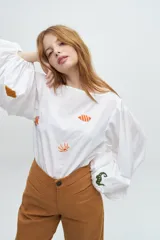 Blusa blanca de algodón con mangas largas voluminosas y escote a la base. Presenta bordados artesanales coloridos con motivos marinos distribuidos en el frente y en las mangas.