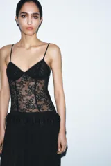 Body de encaje negro con diseño de corsetería, escote en pico y tirantes finos ajustables. Presenta paneles de encaje floral con transparencias y costuras estructuradas.