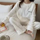 Conjunto de pijama de dos piezas confeccionado en tela de plush texturizada con diseño de rayas verticales en relieve. Incluye una remera de manga larga con cuello redondo y un pantalón de corte holgado. La remera presenta un pequeño bordado decorativo en el pecho.