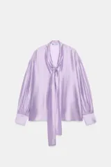 Camisa satinada de manga larga color lila, confeccionada en hilatura con mezcla de lyocell de ZARA Woman Collection. Presenta cuello redondo con escote en pico adornado con lazadas del mismo tejido, mangas abullonadas y puños anchos.