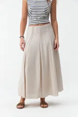 Falda larga beige de corte evasé, con diseño fluido y detalles de costuras verticales en la parte delantera.