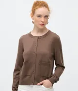 Cardigan de punto color beige, de corte clásico y manga larga, con cuello redondo, cierre frontal por botones y bolsillos delanteros funcionales.