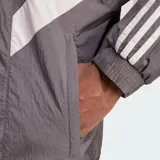 Chaqueta deportiva Adidas del Real Madrid en color gris, con diseño de bloques en blanco y azul marino, cuello alto, cierre frontal y las icónicas tres tiras en las mangas.