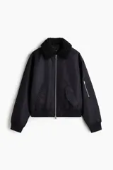 Campera bomber de nylon color negro con corte holgado y levemente acolchada. Cuenta con cuello de peluche al tono, cierre frontal metálico, bolsillos laterales con solapa y un bolsillo con cierre en la manga. Posee puños y bajo acanalados.