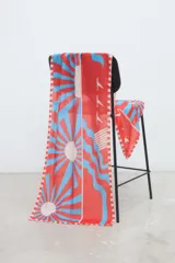 Pareo rectangular estampado con diseño geométrico radial en tonos rojo, celeste y blanco, inspirado en la arquitectura Art Decó. Confeccionado en Uruguay, ideal para usar como falda cruzada, accesorio de playa o chal.