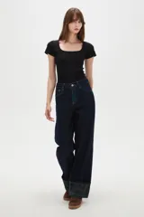 Pantalón de jean azul oscuro de corte recto y tiro alto, con costuras en contraste y dobladillo con vuelta que revela un estampado de cuadros en tonos verdes y azules.