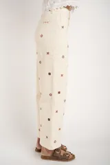 Jean de corte recto y tiro medio, color off-white, con diseño de pequeños bordados en forma de cruz distribuidos por toda la prenda.