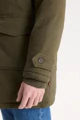 Campera parka larga color verde militar con capucha forrada en piel sintética. Tiene cierre frontal con cremallera y botones a presión, cuatro bolsillos delanteros con solapa y puños ajustables con botones.