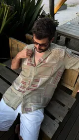 Camisa de manga corta con cuello clásico y estampado geométrico en tonos verde, beige y rojo. Cierre frontal con botones. Corte recto.