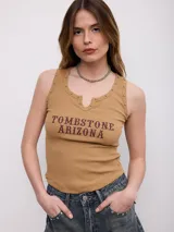 Musculosa de canalé color beige, con escote redondo y pequeña abertura frontal en V. Presenta detalles de tachas metálicas en las sisas y el escote, además de un estampado frontal con la inscripción "TOMBSTONE ARIZONA".