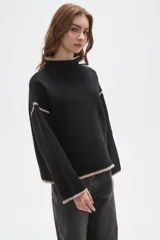 Polera de tejido de punto color negro con detalles de vivos en color beige en el cuello, puños, ruedo y costuras de las mangas. Presenta un diseño holgado con cuello alto y mangas largas.