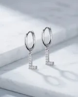 Par de aros de acero quirúrgico tipo argolla con dije colgante en forma de letra con incrustaciones de circonitas.