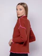 Polera de punto color beige con cuello alto, manga larga y detalles de costura overlock en color naranja.