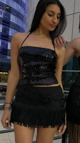 Minifalda short negra de tiro bajo y silueta entallada, con diseño de doble cinturón ancho con hebillas y flecos cortos en el ruedo.