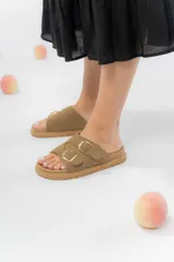Sandalias bajas color beige con dos tiras anchas gamuzadas y hebillas metálicas doradas. Suela acolchada y antideslizante.