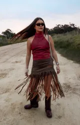Pollera midi de cuero marrón con diseño asimétrico y flecos largos que aportan movimiento y textura.