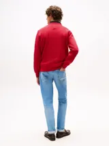 Buzo rojo de cuello redondo con ribetes distintivos, logo texturizado de Tommy Hilfiger en el pecho y logo bordado en la manga. El cuello es azul marino y se asoma un cuello de camisa a rayas. Los puños tienen ribetes distintivos.