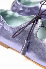 Zapato tipo blucher de piel metalizada en color violeta, con diseño híbrido entre blucher y bailarina. Presenta cierre con cordones y borlas decorativas, acabado sin ribete con ondas laterales y elástico en la parte trasera para un ajuste óptimo. Interior y suela de cuero.