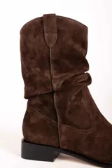 Bota de caña media confeccionada en gamuza color tostado, con diseño arrugado en la caña, punta fina y suela plana con pequeño taco cuadrado.