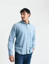Camisa de denim de algodón con cuello clásico, cierre frontal con botones, bolsillo superior de parche y mangas largas con puños abotonados.