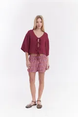 Blusa de lino italiano color beige, de manga corta, con escote en V y cierre frontal mediante lazos o moños.