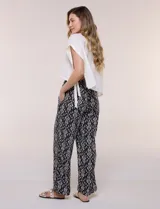 Pantalón wide leg de calce holgado y caída fluida, color negro con estampado de arabescos blancos. Cuenta con cintura elastizada fruncida con lazo ajustable, terminaciones en canutillo de madera y bolsillos laterales funcionales.