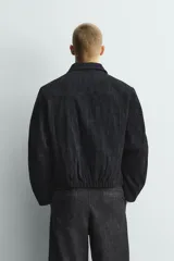 Cazadora de corte regular fit confeccionada en tejido jacquard con textura abstracta. Presenta cuello solapa, cierre frontal de cremallera, bolsillos de vivo en la cadera y mangas largas con puños ajustables mediante botón a presión oculto.