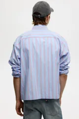 Camisa de corte relajado confeccionada en algodón, con diseño de rayas verticales en tonos azul, blanco y rojo. Presenta cuello americano, cierre frontal con botones, bolsillo en el pecho y mangas largas con puños abotonados.
