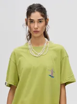 Remera de corte cuadrado y ajuste holgado, color verde oliva, con pequeño estampado gráfico de un velero en el pecho y etiqueta decorativa en la manga.