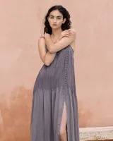 Vestido largo negro con tirantes finos ajustables, cuerpo con plisado fino y detalle de hilera de botones decorativos en el lateral. Cuenta con una falda amplia y fluida con abertura lateral.