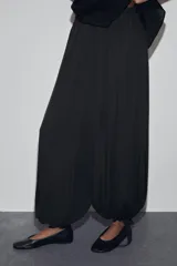 Pantalón bombacho de tiro alto con cintura elástica, confeccionado en tejido fluido con acabado satinado. Presenta un diseño holgado con bajo acabado en puño elástico y detalle de lazada ajustable.