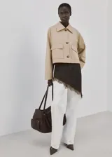 Chaqueta corta de algodón en color beige, con cuello camisero, mangas largas, dos bolsillos con solapa en el frente y cierre de botones.