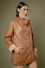 Campera de cuero color tostado con diseño de paneles, cuello alto y puños con forro de corderito sintético. Presenta cierre frontal con botones grandes y bolsillos laterales.