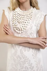 Vestido largo de crochet color crudo, con mangas cortas con volados y aberturas laterales, confeccionado en tejido calado de algodón con diseño ornamentado.