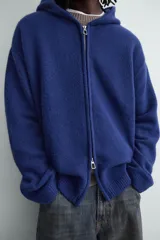 Chaqueta de punto de corte relajado, color azul, con capucha, cierre frontal con cremallera y acabados en rib en puños y bajo.