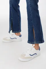 Zapatillas blancas con detalles en gamuza beige y una franja ondulada azul en el lateral. Tienen cordones blancos y suela plana.