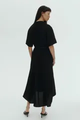 Vestido midi negro con cuello camisero, mangas cortas y botones ocultos. Incluye un cinturón fino con hebilla metálica dorada en la cintura y falda evasé de corte midi.