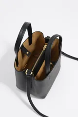 Bolso pequeño de piel color borgoña, con estructura rígida y forma de cubo. Posee doble asa de mano y una correa larga para llevar al hombro o cruzado. El frente lleva el logo metálico de Bimba y Lola.