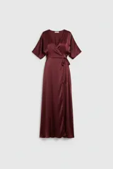 Vestido largo tipo kimono confeccionado en satén color bordó, con escote en V cruzado, mangas amplias y lazo ajustable en la cintura. Presenta una falda fluida con abertura lateral.