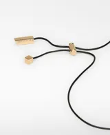 Collar de cordón largo ajustable con piezas metálicas bicolor, combinando un dije plateado y uno dorado con diseño orgánico. Posee terminal logotipado en color dorado.