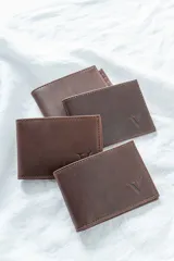 Billetera de cuero pull up engrasado color chocolate, con logo grabado en la esquina inferior derecha. Diseño plegable con múltiples compartimentos para tarjetas y billetes.
