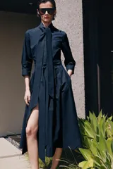 Vestido midi de algodón con cuello con lazada, manga tres cuartos y falda evasé. Incluye cinturón ajustable del mismo tejido y cierre frontal con botones.