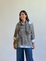 Sweater de punto color visón con diseño superpuesto, que incluye una bufanda integrada y detalles de encaje floral en el frente. Presenta mangas tres cuartos con puños abotonados y un corte holgado.