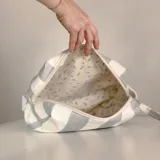 Neceser rectangular de tela a rayas verticales blancas y celestes, con cierre superior y etiqueta de cuero con logo de la marca.