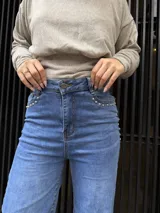 Pantalón de jean azul de corte recto y tiro alto, con detalle de tachas metálicas en los bolsillos delanteros y cierre frontal con botón.