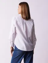 Camisa blanca de algodón con cuello clásico, escote en V y cierre frontal con botones. Presenta apliques de brillos plateados en el frente y mangas largas con puños abotonados.