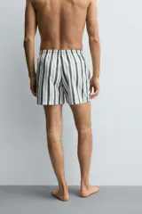 Bañador de hombre de tejido técnico con estampado de rayas verticales en verde oscuro, azul claro y blanco. Presenta cintura elástica ajustable con cordón blanco, bolsillos laterales y un bolsillo trasero de vivo.