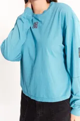 Remera celeste de manga larga, corte holgado y largo a la cadera. Tiene el logo de la marca bordado y pespuntes a contratono.