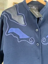 Campera tejida de lana color azul marino, de corte recto y manga larga, con cuello mao y detalles de apliques de cuero en los hombros.