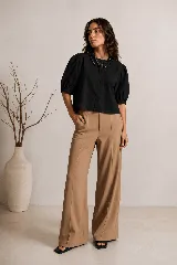 Blusa negra de corte estructural con mangas cortas abullonadas con tablas, cartera oculta con botones de nácar y cuello redondo.